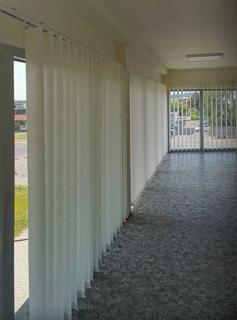 Bílé látkové vertikální žaluzie instalované na velkých oknech